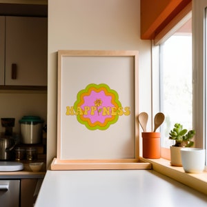 May include: A framed vertical print featuring the word HAPPINESS in yellow block letters. The text is centered over a pink, orange, and lime green scalloped circular graphic with a small yellow flower illustration replacing the letter I.