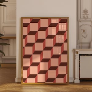 Könnte beinhalten: Ein gerahmter Kunstdruck mit einem optischen Täuschungsdesign aus abwechselnden 3D-Würfeln in Rosa- und Brauntönen. Das Kunstwerk ist in einem goldfarbenen Rahmen eingefasst und schafft eine moderne und geometrische Ästhetik. Der Druck wird vor einer weißen Wand präsentiert.