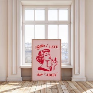 Pu&ograve; includere: Un poster rosa e rosso con un'illustrazione retr&ograve; di una donna che si applica il rossetto. Il testo sul poster recita "Meglio tardi che mai."
