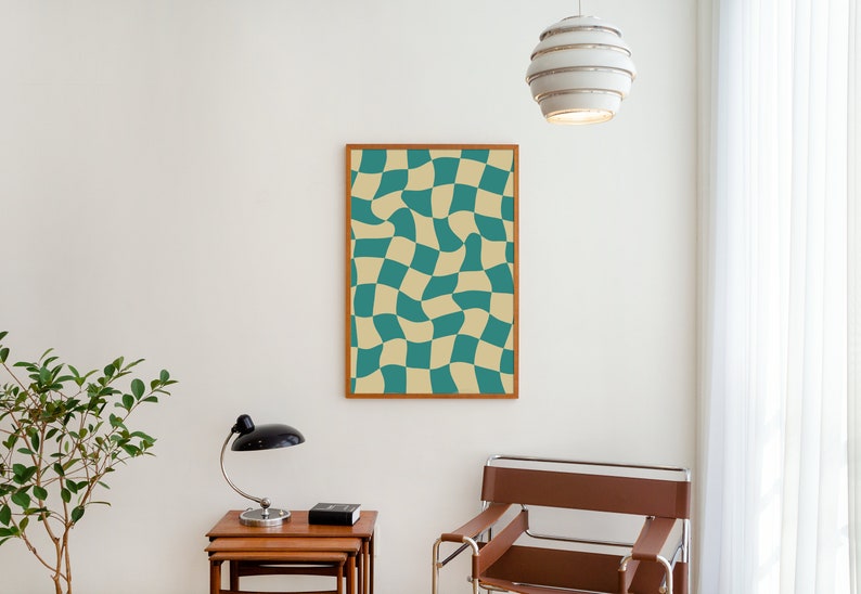 May include: A framed print of a checkered pattern with teal and beige squares. The squares are distorted, creating a wavy effect. The print is hanging on a white wall in a room with a wooden table, a lamp, and a chair.