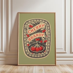 May include: Framed vintage-style print featuring a decorative label for "Cherry Brandy." The design includes a central oval with red cherries, a banner with the text "Cherry Brandy," and ornate black and cream-colored borders.
