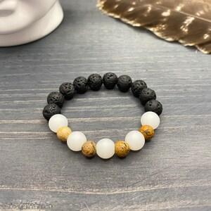May include: A black and white beaded bracelet with brown accents. The bracelet is made of lava rock, white jade, and brown jasper beads.