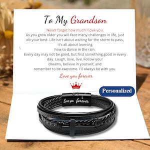 May include: A black leather bracelet with a cross charm and a silver clasp. The bracelet has the words "Love you forever" engraved on the clasp. The bracelet is on a white card with a message to a grandson.