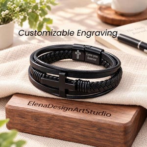 May include: A black leather multi-strand bracelet featuring a central black cross charm and a black metal clasp engraved with a cross symbol and the text Love you forever. The bracelet combines smooth leather cords with braided leather sections.