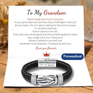 May include: A black leather bracelet with a silver knot design and a silver clasp. The clasp has an infinity symbol and the words "Love you forever" engraved on it. The bracelet is on a white card with the words "To My Grandson" and a message about life and love. The card also has a crown and the word "Personalized" on it.