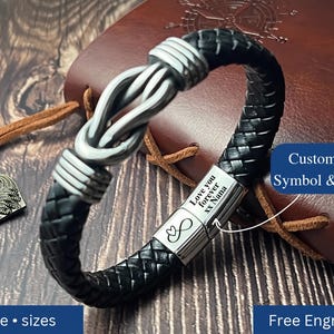 May include: A black braided leather bracelet featuring a silver-toned metal knot centrepiece and a rectangular clasp engraved with the text Love you forever xx Nana and an infinity symbol with a heart. The bracelet includes a metal anchor charm.