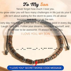 May include: A wooden bracelet with metal accents and a black cord. The bracelet has a message in Morse code that reads "I love you".