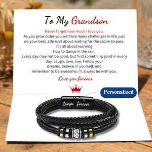 May include: A black leather bracelet with a silver clasp and a message that reads "Love you forever". The bracelet is on a card with a message to a grandson. The card reads "To My Grandson, Never forget how much I love you... Love you forever".