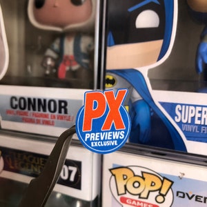 May include: A red and white circular sticker with the text "PX Previews Exclusive" on a white background. The sticker is attached to a clear plastic box with a Funko Pop! figure inside.
