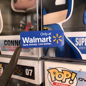 May include: A blue and yellow sticker with the Walmart logo and the text "Only at Walmart Save money. Live better."  The sticker is attached to a clear plastic display case with a blue and black Batman Pop! figure inside.