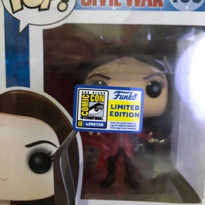 May include: A Scarlet Witch vinyl bobble-head figure from the Marvel Captain America Civil War series, number 133. The figure is in its original packaging, with a Comic-Con International Limited Edition sticker.