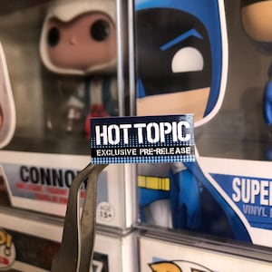 May include: A blue and white sticker with the text "HOT TOPIC EXCLUSIVE PRE-RELEASE" on a blue and yellow background.