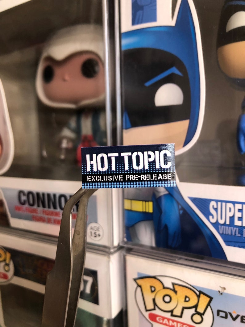 May include: A blue and white sticker with the text "HOT TOPIC EXCLUSIVE PRE-RELEASE" on a blue and yellow background.