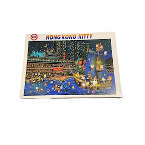 May include: A rectangular jigsaw puzzle box featuring a night scene of Hong Kong with the text HONG KONG KITTY and JUMBO. The illustration depicts a large traditional boat with a blue sail, a green dragon, and various cartoon characters on water.