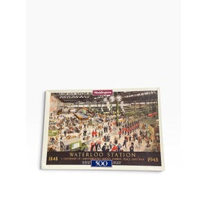 May include: A rectangular Waddingtons 500-piece jigsaw puzzle box featuring a detailed illustration of Waterloo Station. The scene depicts a busy train station with crowds, soldiers in red uniforms, and the text Waterloo Station 1848-1948.