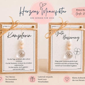 May include: Two rectangular kraft paper cards in clear plastic sleeves, each featuring a hanging clear faceted glass bead, wooden beads, and a jute twine bow. The cards display German text, including the words K&auml;mpferin and Gute Besserung.