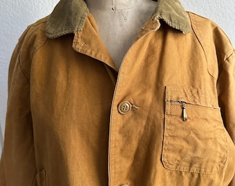 May include: A brown canvas jacket with a corduroy collar. The jacket has a zipper and button closure, and a small pocket on the chest. The label on the jacket reads "Superior Model Forms Co."