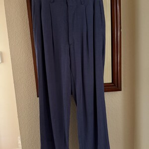 K&ouml;nnte beinhalten: Marineblaue Hose mit Falten, h&auml;ngt an einem Holzb&uuml;gel. Die Hose hat eine lockere Passform mit umgeschlagenem Saum. Die Hose ist aus leichtem Stoff und scheint in gutem Zustand zu sein.