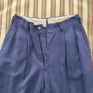 K&ouml;nnte beinhalten: Blaue Hose mit hohem Bund und Rei&szlig;verschluss. Die Hose hat Falten vorne und G&uuml;rtelschlaufen. Der Stoff scheint ein strukturiertes, gewebtes Material zu sein.