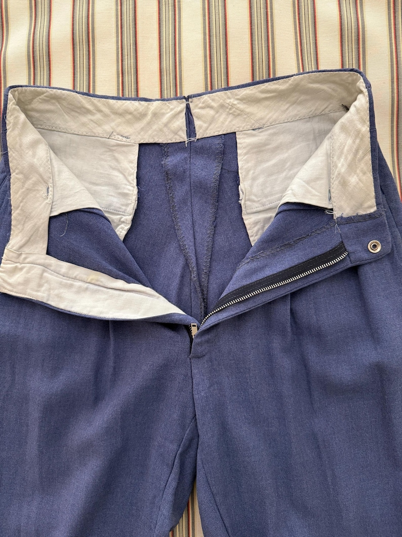 K&ouml;nnte beinhalten: Nahaufnahme einer blauen Hose mit Rei&szlig;verschluss und Knopfverschluss. Die Hose hat ein wei&szlig;es Futter am Bund und Falten vorne. Der Stoff scheint ein mittelschweres Material zu sein.