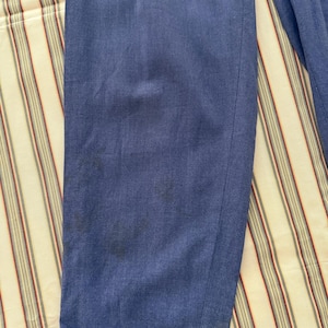 K&ouml;nnte beinhalten: Nahaufnahme einer blauen Hose mit umgeschlagenem Saum. Der Stoff weist einige dunkle Flecken auf und scheint ein mittelschweres Material zu sein. Die Hose liegt auf einem gestreiften Stoff.