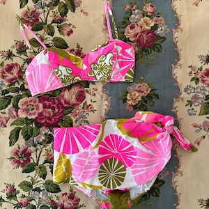 May include: A pink and green floral print bikini top and bottom. The top has a sweetheart neckline and adjustable straps. The bottom is a high-waisted style with a tie at the side.