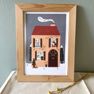May include: A framed illustration of a house with a red roof and snow on the ground. The house has windows with people looking out, a Christmas tree, and a dog. The illustration is in a light wood frame.