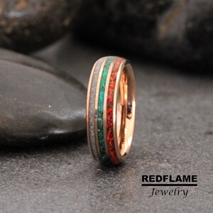 May include: A rose gold ring with a white, green, and red inlay. The ring has a polished finish and is set with small red gemstones.