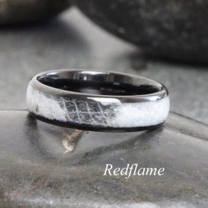 May include: A black ring with a white and gray patterned inlay. The ring has a polished finish and is set against a dark background. The text "Redflame" is at the bottom of the image.