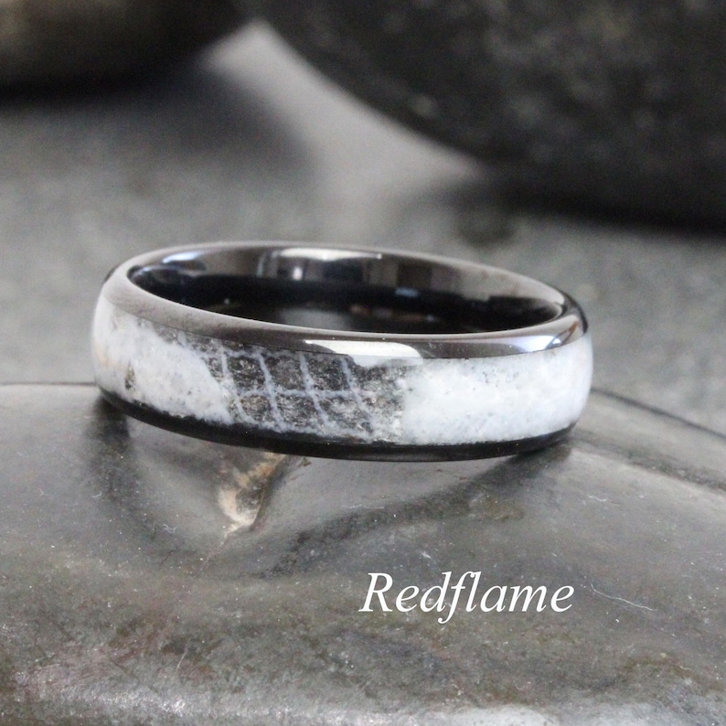 May include: A black ring with a white and gray patterned inlay. The ring has a polished finish and is set against a dark background. The text "Redflame" is at the bottom of the image.