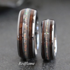 May include: Two matching rings with a wood grain pattern and a central band of iridescent material. The rings have a polished metal exterior and the word "Redflame" is printed at the bottom.
