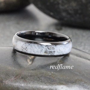 May include: A black ring with a white, textured inlay. The ring has a polished finish and is set against a dark background. The text "redflame" is in the lower right corner.