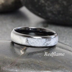 May include: A black ring with a white and gray marbled inlay. The ring has a polished finish and is set against a dark background. The text "Redflame" is visible on the ring.