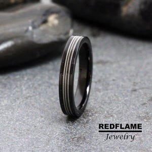 May include: A black and silver wedding band with a grooved design. The band is made of metal and has a polished finish.
