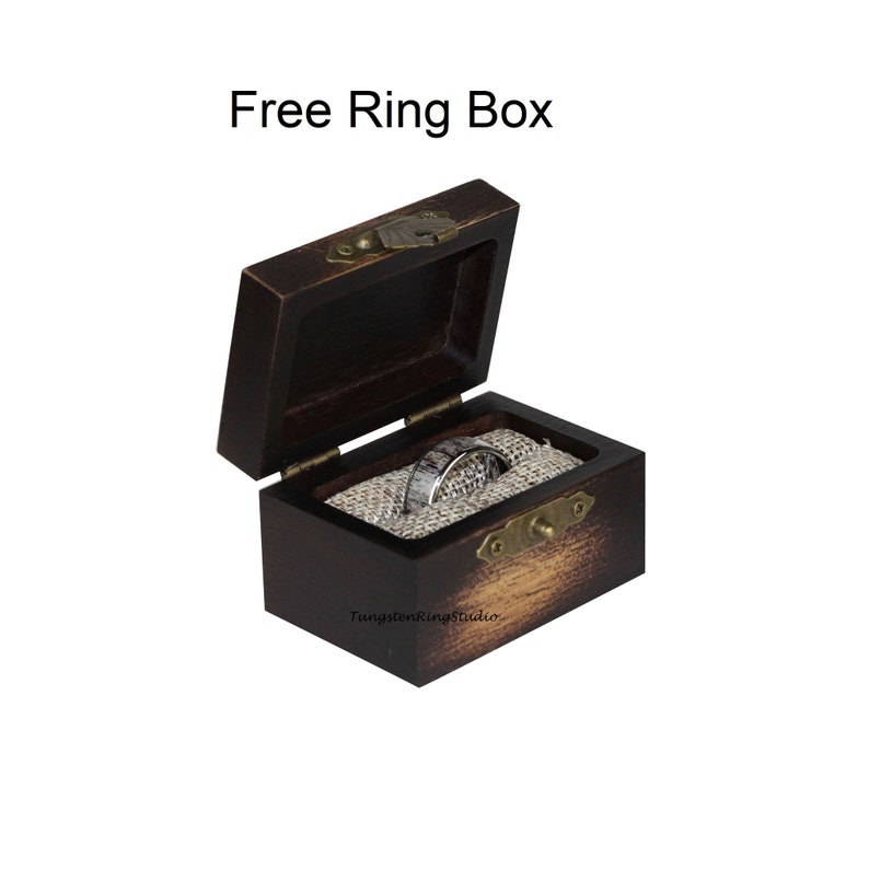 May include: A dark brown wooden ring box with a hinged lid, open to reveal a silver ring on a burlap-like fabric. The box has a brass clasp and hinges. Text on the box reads "Free Ring Box".