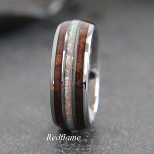 May include: A silver ring with a wood grain and opal inlay. The ring has a polished finish. The text "Redflame" is visible at the bottom. The ring's design is visible in close-up.