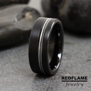 May include: A black tungsten carbide ring with two silver-colored grooves around the band.  REDFLAME Jewelry.
