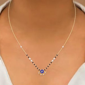 May include: A gold chain necklace with a blue evil eye charm surrounded by white and black gemstones.