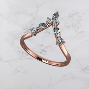 Może przedstawiać: Złoty pierścionek w kolorze różowego złota z wzorem w kształcie litery V ozdobiony małymi, przezroczystymi kamieniami szlachetnymi.