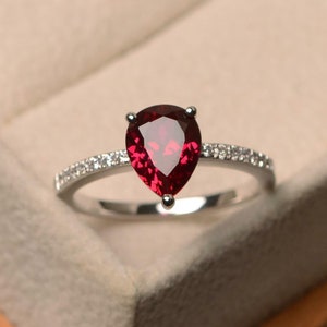 May include: A pear-shaped ruby ring with a silver band and a row of small diamonds around the centre stone.