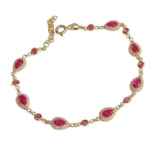 May include: A gold-toned bracelet featuring alternating teardrop-shaped and round red gemstones. The teardrop gems are surrounded by small, clear stones. The bracelet has a delicate chain and a clasp closure. A piece of jewelry.