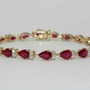 May include: Gold bracelet with pear-shaped red gemstones and small white diamonds. The bracelet has a secure clasp and is set on a gold chain. The gemstones are evenly spaced along the bracelet.