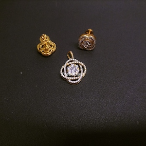 Puede incluir: Un conjunto de joyas de oro que incluye un colgante y pendientes. El colgante es de diseño circular con una piedra grande transparente en el centro rodeada de piedras transparentes más pequeñas. Los pendientes son de diseño similar pero más pequeños.