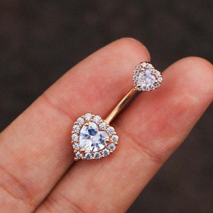 May include: A rose gold belly button ring with two heart-shaped clear crystal stones.