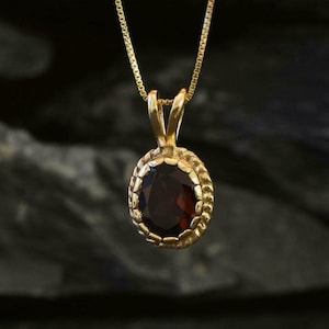 May include: A gold chain necklace with a pendant featuring a dark red gemstone set in a gold bezel.
