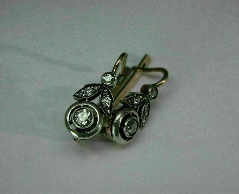 May include: A pair of silver and gold earrings with a floral design and clear gemstones.