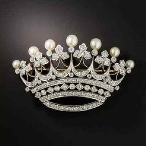 May include: A silver-coloured crown brooch, intricately designed with clear gemstones and large, round, white pearls. The crown's ornate details are set against a black backdrop, showcasing its elegant design.