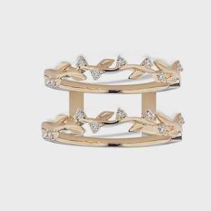 Può includere: Un anello doppio in oro con un design a forma di tralcio di vite su ogni fascia. Le fasce sono collegate da due barre verticali in oro. Ogni segmento del tralcio è decorato con piccole pietre rotonde trasparenti incastonate sui rami.