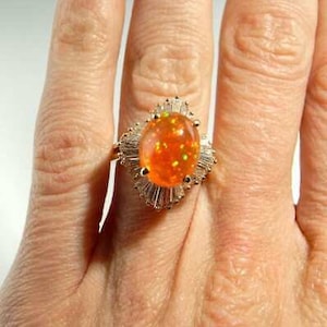 May include: A gold ring with a large oval orange opal surrounded by a halo of small diamonds.