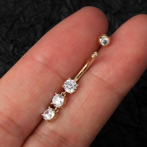 May include: Gold belly button ring with three clear round cubic zirconia stones.